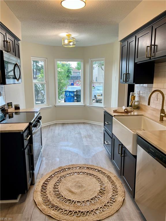 kitchen with stainless steel appliances, a sink, backsplash, plenty of natural light, and a textured ceiling