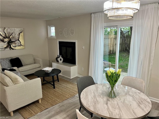 living area featuring wood finished floors, a textured ceiling, a glass covered fireplace, baseboards, and a chandelier