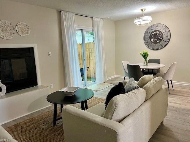 living area featuring light wood-style flooring, a glass covered fireplace, a textured ceiling, and baseboards