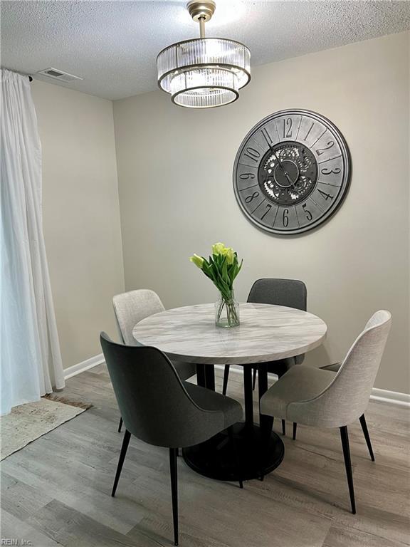 dining room with wood finished floors, a textured ceiling, baseboards, and a chandelier