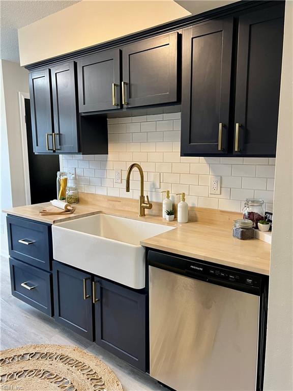kitchen with stainless steel dishwasher, a sink, decorative backsplash, light countertops, and a textured ceiling
