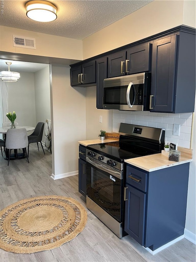 kitchen featuring stainless steel appliances, light wood-style flooring, light countertops, backsplash, and a textured ceiling