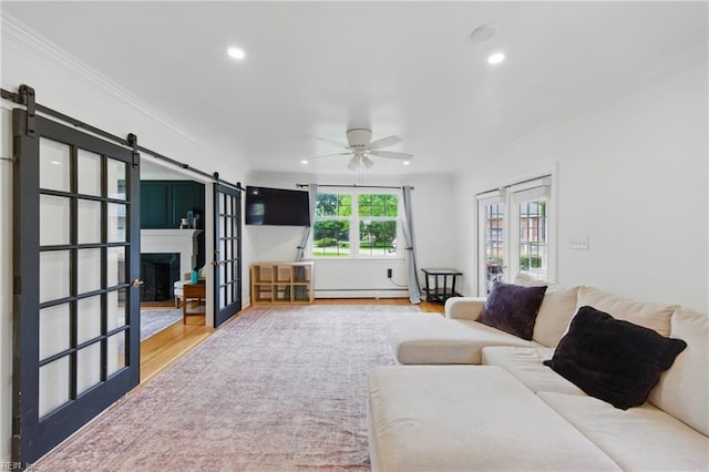 living area featuring a barn door, a baseboard radiator, ceiling fan, ornamental molding, and recessed lighting