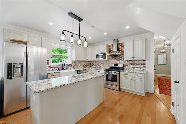 kitchen with appliances with stainless steel finishes, wall chimney range hood, a sink, white cabinets, and recessed lighting