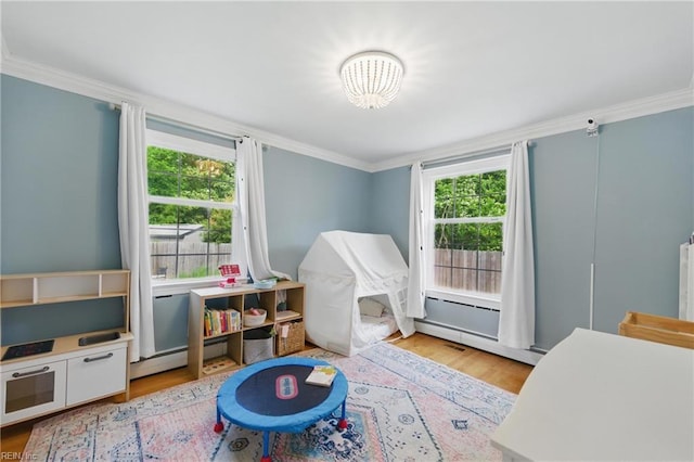 rec room featuring healthy amount of natural light, ornamental molding, light wood-style floors, a chandelier, and baseboard heating