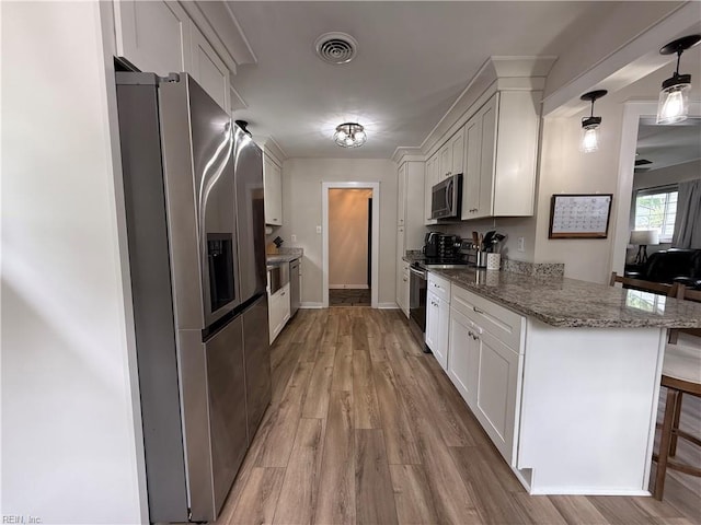 kitchen with stainless steel appliances, light wood finished floors, white cabinetry, and light stone countertops