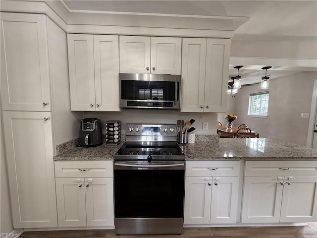 kitchen with appliances with stainless steel finishes, white cabinetry, a peninsula, and light stone counters