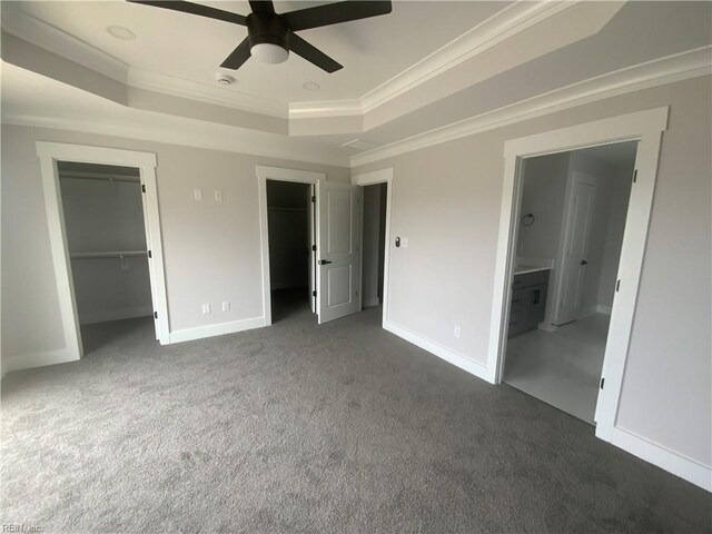 unfurnished bedroom with a tray ceiling, ornamental molding, dark colored carpet, a spacious closet, and baseboards