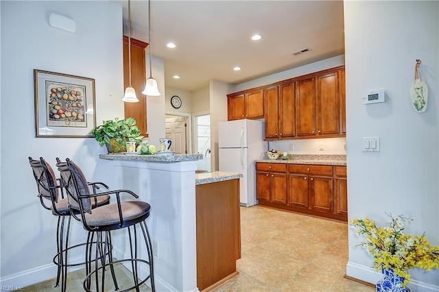 kitchen with freestanding refrigerator, a kitchen bar, a peninsula, brown cabinets, and recessed lighting