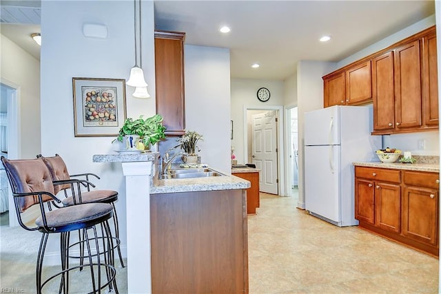 kitchen with freestanding refrigerator, a sink, a breakfast bar area, brown cabinets, and recessed lighting