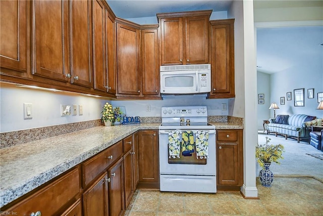 kitchen featuring white appliances, brown cabinetry, and light stone countertops