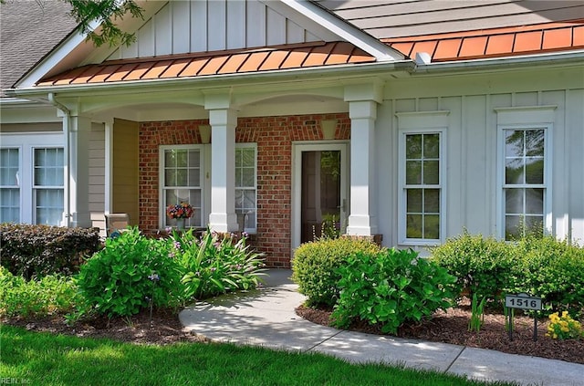 doorway to property featuring board and batten siding, brick siding, a porch, and a standing seam roof