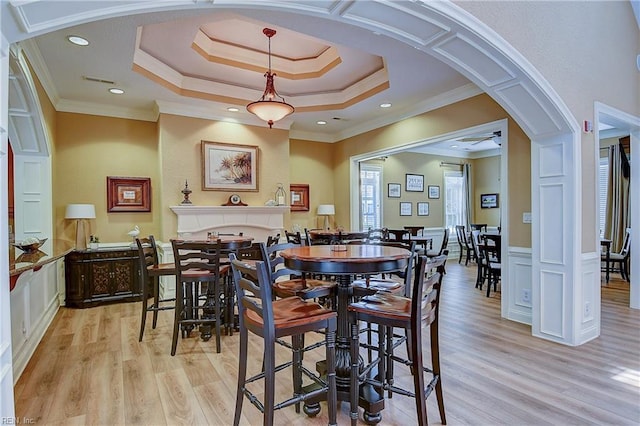 dining space featuring light wood finished floors, ornamental molding, a tray ceiling, arched walkways, and recessed lighting