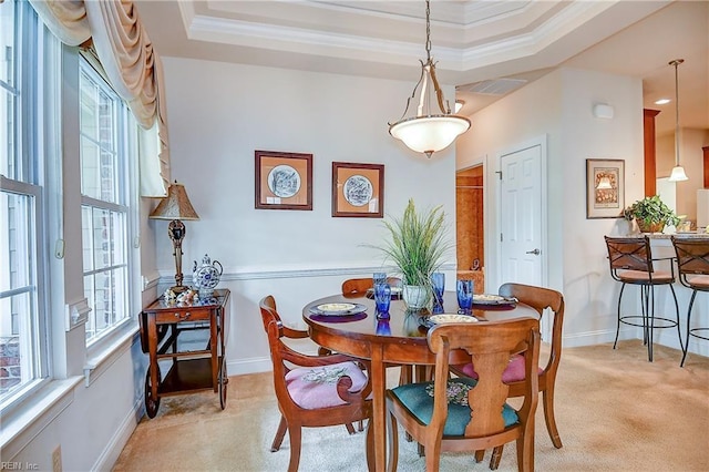 dining room featuring light colored carpet, plenty of natural light, a raised ceiling, ornamental molding, and baseboards