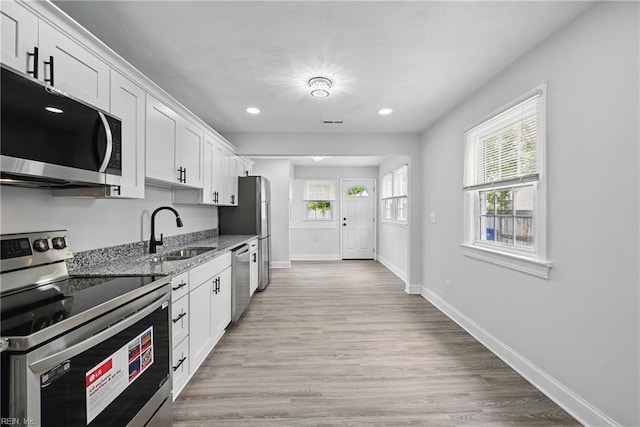 kitchen with stainless steel appliances, a sink, light stone counters, white cabinetry, and recessed lighting