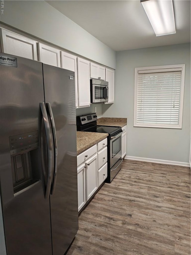 kitchen featuring stainless steel appliances, wood finished floors, white cabinetry, baseboards, and light stone counters