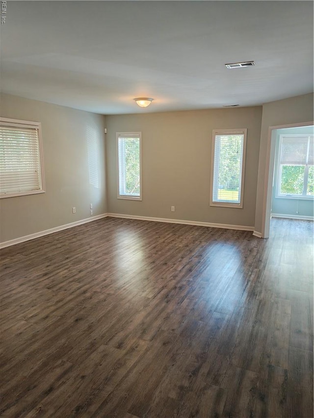 spare room with dark wood-style flooring, plenty of natural light, and baseboards
