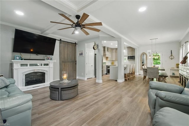 living area featuring a barn door, light wood-style floors, crown molding, baseboards, and ceiling fan