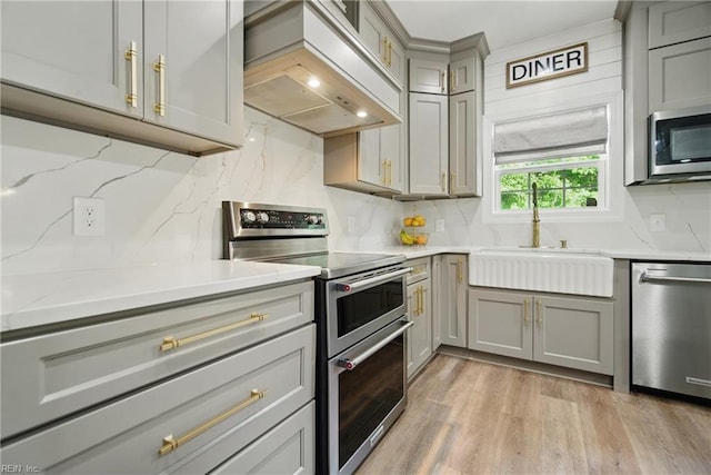 kitchen with stainless steel appliances, a sink, gray cabinets, premium range hood, and tasteful backsplash