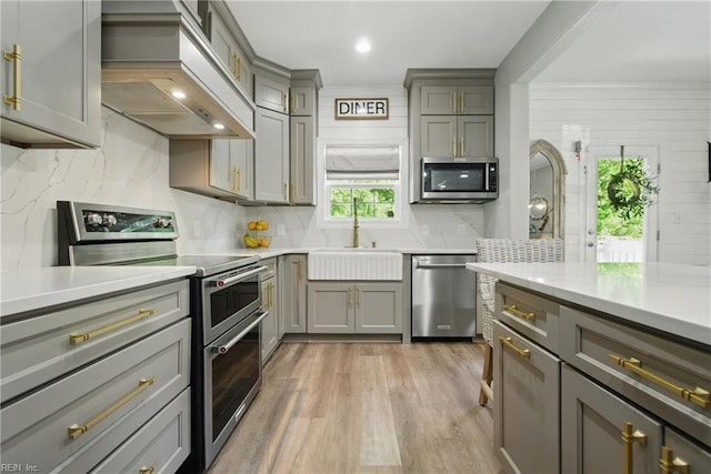 kitchen featuring stainless steel appliances, a sink, gray cabinets, custom exhaust hood, and backsplash