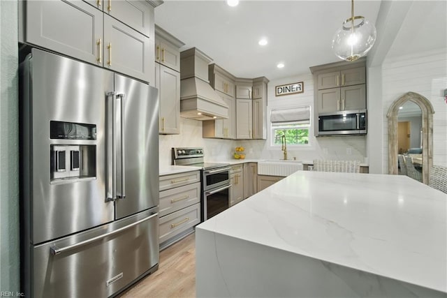 kitchen with appliances with stainless steel finishes, custom exhaust hood, gray cabinetry, a sink, and light wood-type flooring
