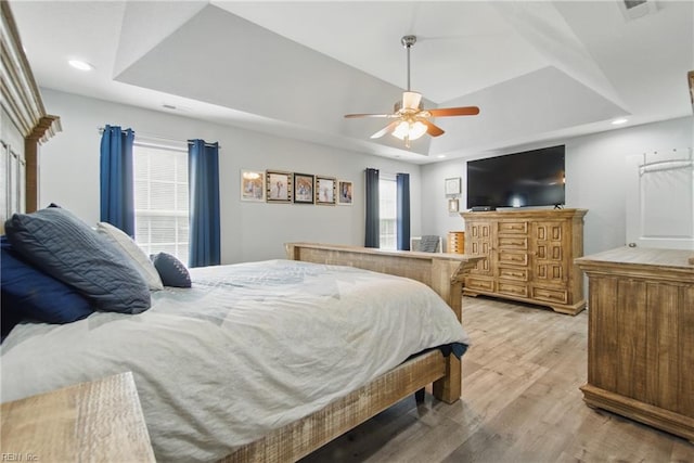 bedroom with a raised ceiling, light wood-type flooring, recessed lighting, and ceiling fan