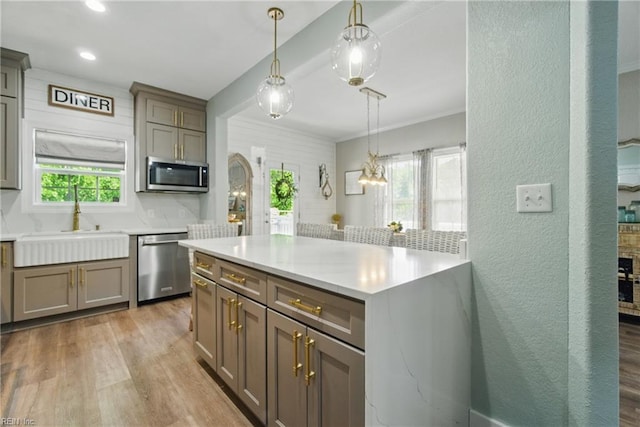 kitchen featuring appliances with stainless steel finishes, a sink, light wood finished floors, decorative light fixtures, and light countertops