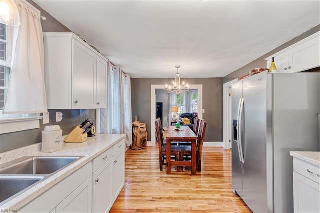 kitchen featuring stainless steel fridge, a chandelier, light wood-style flooring, white cabinetry, and a sink