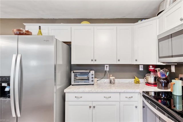 kitchen featuring appliances with stainless steel finishes, white cabinets, and light stone counters