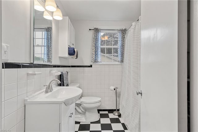 bathroom with toilet, tile patterned floors, tile walls, vanity, and wainscoting