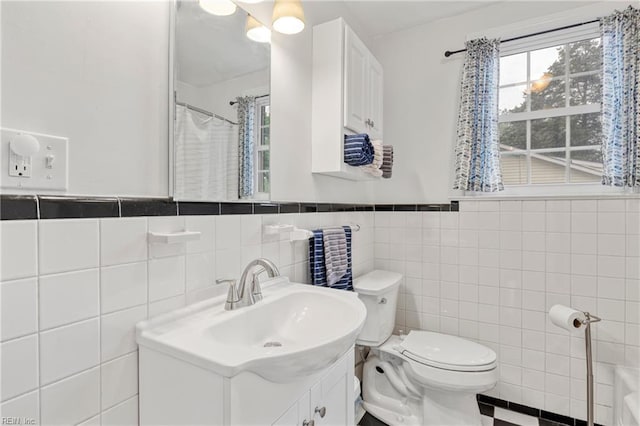bathroom with toilet, tile walls, vanity, and wainscoting