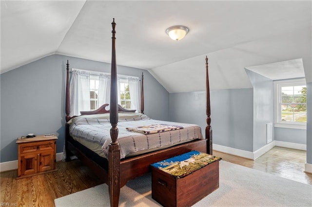 bedroom with lofted ceiling, multiple windows, baseboards, and wood finished floors