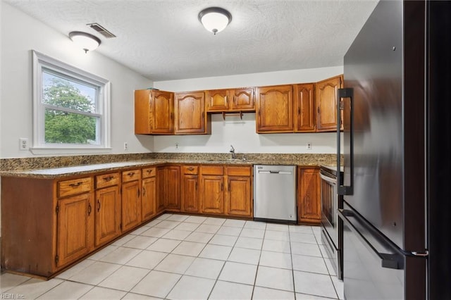 7103 Orcutt Ave, Newport News, VA 23605 - kitchen with stainless steel appliances, a sink, brown cabinetry, a textured ceiling, and dark countertops