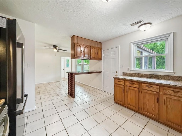 7103 Orcutt Ave, Newport News, VA 23605 - kitchen with brown cabinetry, a ceiling fan, plenty of natural light, light tile patterned flooring, and a textured ceiling
