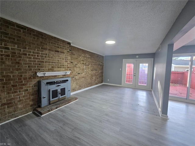 unfurnished living room with a textured ceiling, baseboards, wood finished floors, french doors, and brick wall