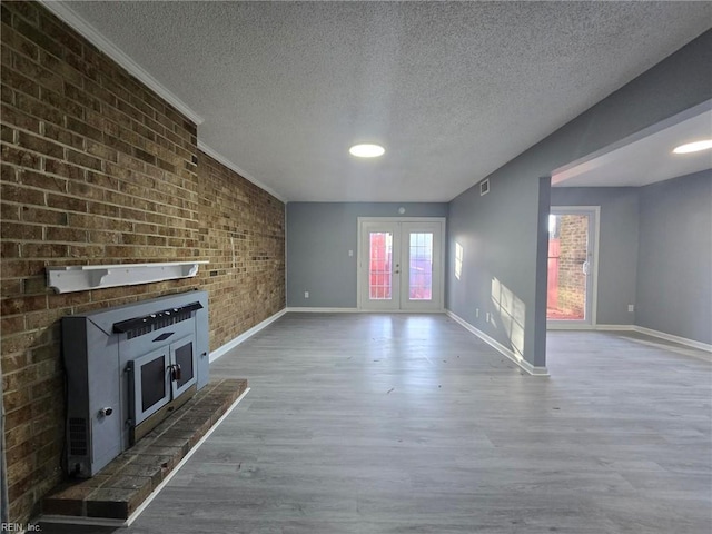 unfurnished living room with french doors, brick wall, baseboards, a textured ceiling, and wood finished floors
