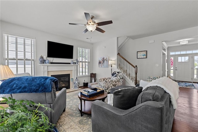 living area with stairway, a ceiling fan, wood finished floors, and a fireplace with flush hearth