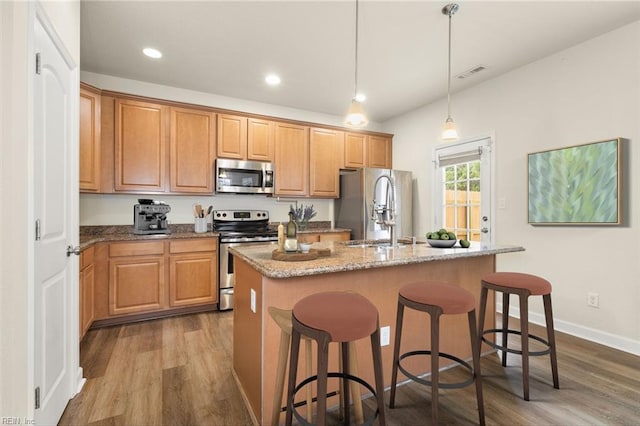 kitchen with appliances with stainless steel finishes, dark wood-style flooring, a center island with sink, a kitchen breakfast bar, and recessed lighting