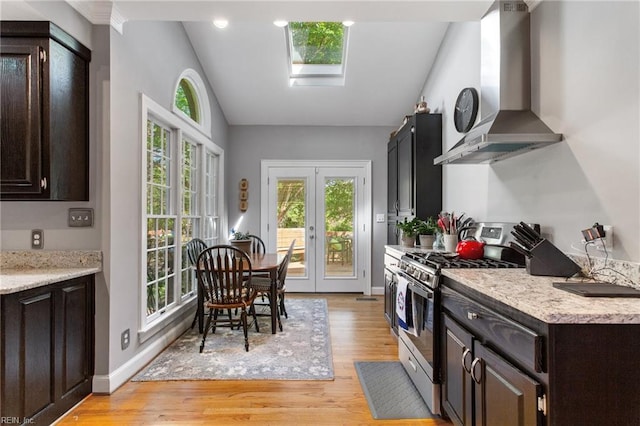 kitchen with stainless steel gas range oven, wall chimney exhaust hood, vaulted ceiling, light wood-style flooring, and healthy amount of natural light