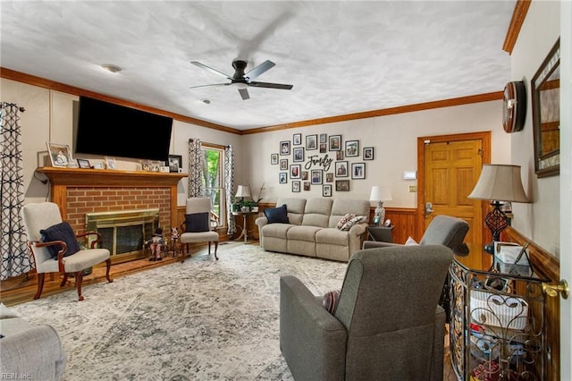 living room featuring ceiling fan, crown molding, wood finished floors, a fireplace, and a wainscoted wall