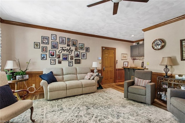 living area featuring wood finished floors, ceiling fan, wainscoting, crown molding, and wood walls