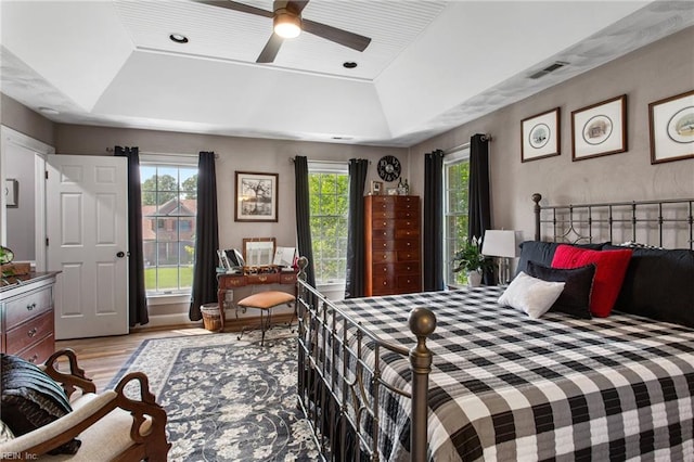 bedroom with a raised ceiling, wood finished floors, and ceiling fan