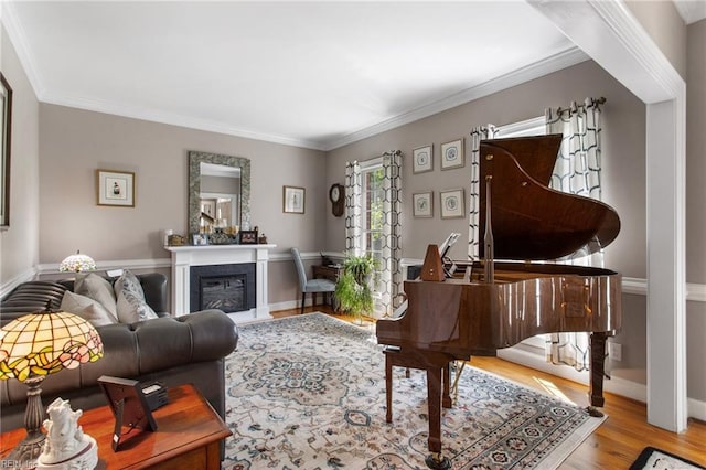 living area featuring ornamental molding, wood finished floors, a glass covered fireplace, and baseboards