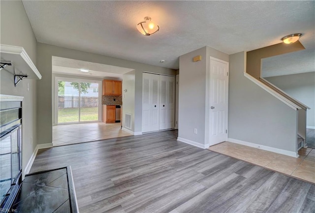 913 Fluvanna Rd, Newport News, VA 23601 - unfurnished living room with light wood finished floors, baseboards, a textured ceiling, a fireplace, and stairway