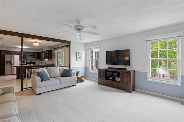 living area with light carpet, baseboards, and a ceiling fan