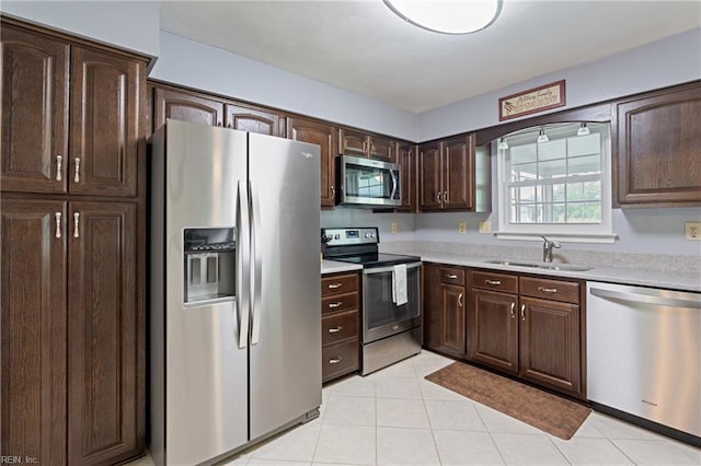kitchen with stainless steel appliances, a sink, light countertops, dark brown cabinetry, and light tile patterned flooring