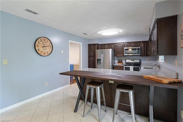kitchen featuring stainless steel appliances, a sink, dark brown cabinets, a peninsula, and baseboards