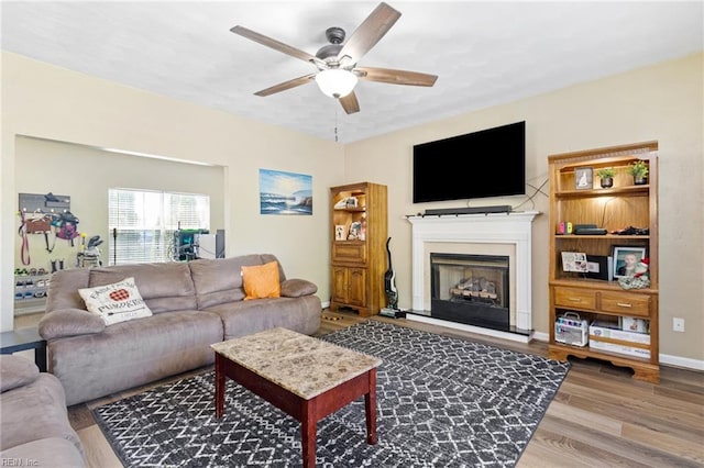 living room with a ceiling fan, wood finished floors, a fireplace with raised hearth, and baseboards
