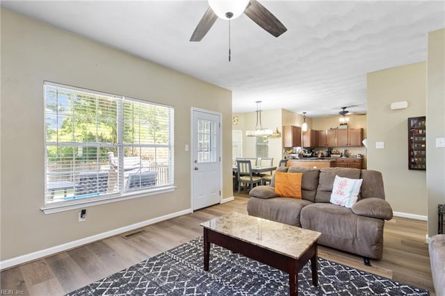 living area featuring ceiling fan, light wood-style floors, and baseboards