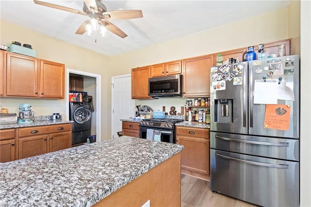 kitchen featuring appliances with stainless steel finishes, a ceiling fan, light stone counters, and light wood-style floors